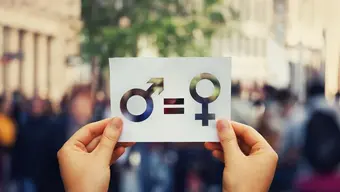 image of two hands holding a card with icons of two genders being equal with a group of people in the background