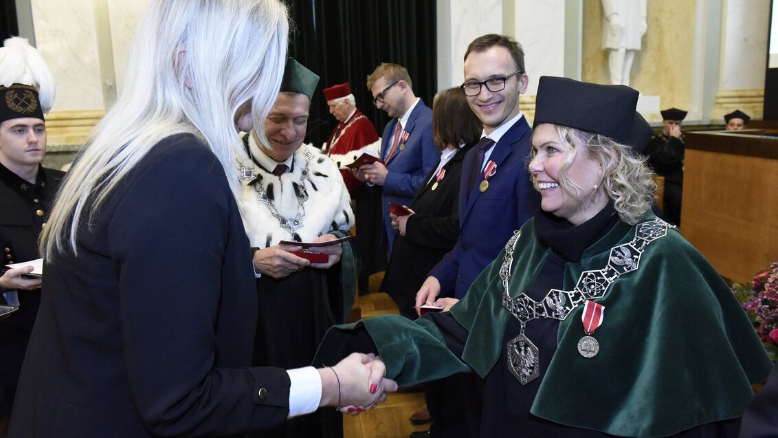 Image of two women shaking hands, one being awarded with a medal, the university rector and another men smiling and standing in the background