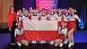 A group of cheerleaders in white and red uniforms posing for a photograph holding a Polish flag with their coach standing to the left.