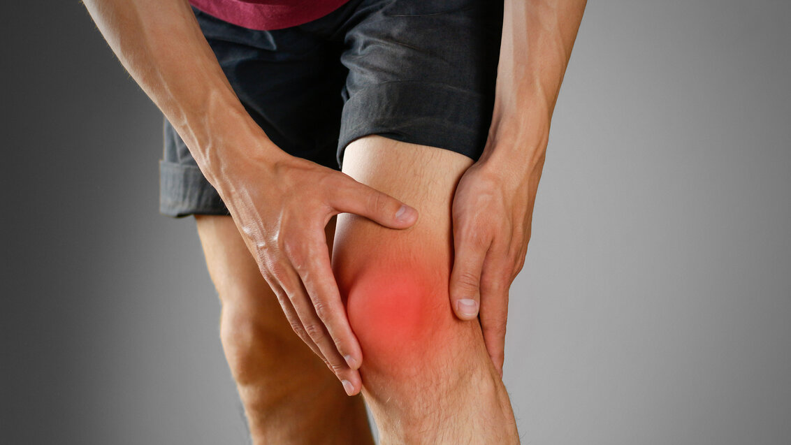 Image of a person in shorts holding their knee which is lit up in red