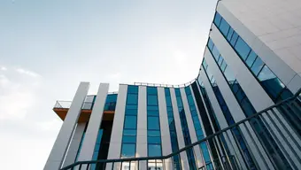 Low-angle view of a modern building with tall white vertical panels and large blue-tinted glass windows.