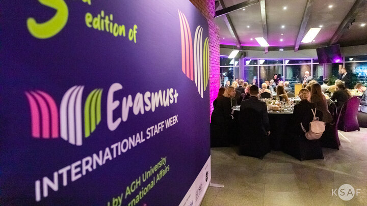 Image of people sitting at round tables next to a large panel of the Erasmus+ International Staff Week