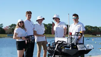 Image of the AGH Solar Boat team with their boat in front of a body of water during a sunny day