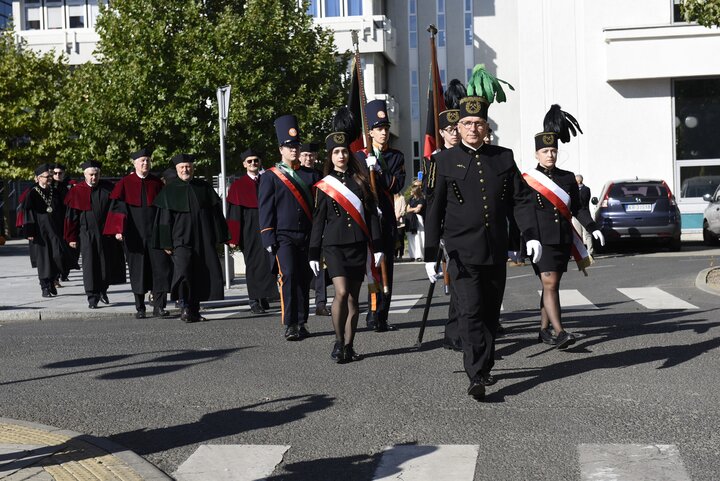 Musicians of the University Orchestra walking down a main campus avenue