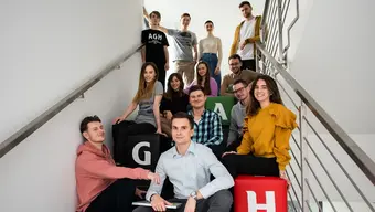 An image of a group of students sitting on a staircase, smiling, posing for a photo with branded AGH University poufs.