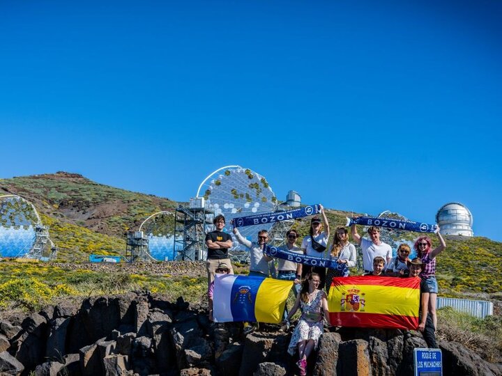  Group of visitors holding flags in front of observatory telescopes on a sunny hillside.