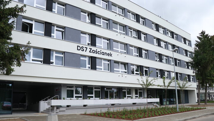 Zdjęcie fragmentu budynku. Elewacja białe poziome pasy. Pomiędzy piętrami napis „DS 7 Zaścianek”