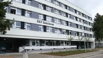 Zdjęcie fragmentu budynku. Elewacja białe poziome pasy. Pomiędzy piętrami napis "DS 7 Zaścianek"