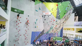 Zdjęcie z zawodów. Po stromej, niemal pionowej ściance wspina się dwóch zawodników. Poniżej widać publiczność.