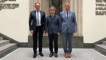 The photo was taken in the Hall of the AGH UST Main Building. It shows three men standing next to each other. They wear suits. Behind them is a statue of Stanisław Staszic.