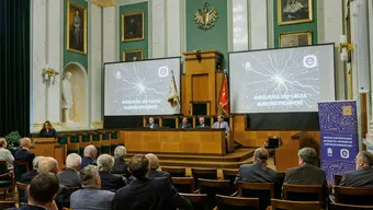 Aula AGH. W rzędach krzeseł siedzą uczestnicy uroczystości. W stallach zasiada Rektor AGH oraz władze Wydziału EAIiIB. Za ich plecami dwa duże ekrany prezentujące grafikę z napisem „Jubileusz 100-lecia Elektrotechniki”.