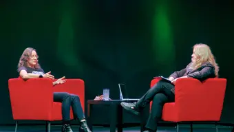 Dwie kobiety siedzą na czerwonych fotelach zwrócone twarzami do siebie