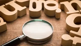 Illustrative image. Scattered letters and a magnifying glass on a table.