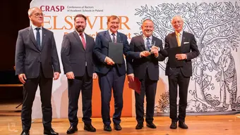 Image of five men with some of them holding folders and an award in front of a photo wall with Elsevier logo
