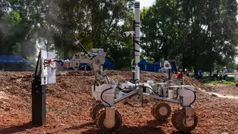 The Kalman rover carrying out a task on the Mars Yard. Brown ground, trees in the background.