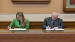 Na zdjęciu moment podpisywania porozumienia przez przedstawicieli obu stron. Sygnatariusze siedzą za stołem, przed każdym z nich dokumenty, które podpisują. Zdjęcie wykonane w sali konferencyjnej.