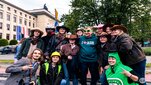 AGH University Rector in an AGH University sweatshirt posing for a photograph with a group of students wearing various costumes. The main building of AGH University is visible in the background.