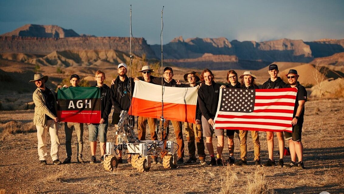 Students on a desert with flags of the AGH UST, Poland, and the United States of America.