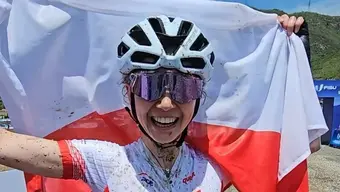 A young woman in a cycling helmet and glasses, smiling, holding a Polish flag.