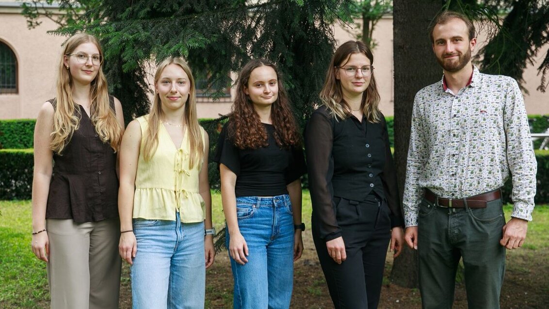Four women and a man posing for a photo standing outside of a buillding.
