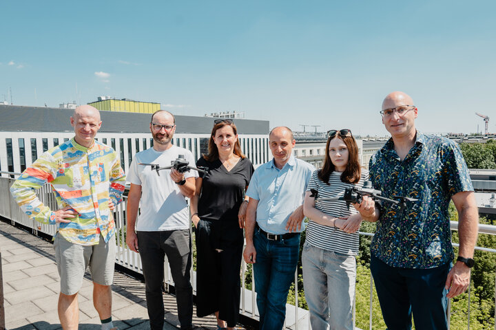 Six people posing for a photo on a rooftop. Two of them are holding drones.