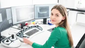 Image of a student sitting at three monitors with an advanced keyboard and joysticks on the desk