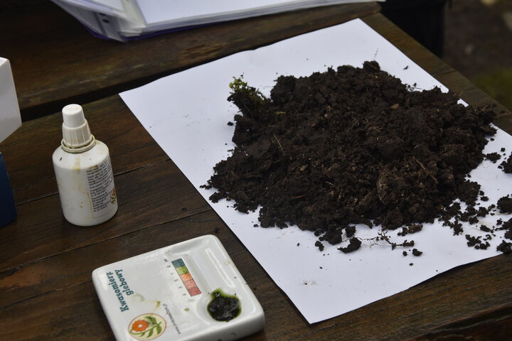 A soil sample on a white sheet of paper next to a soil pH meter.