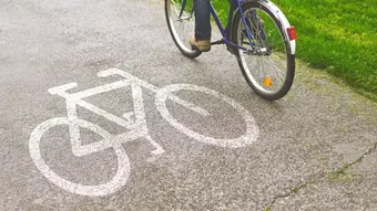 Person riding a blue bicycle on a paved bike path marked with a white bicycle symbol.