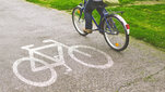 Person riding a blue bicycle on a paved bike path marked with a white bicycle symbol.