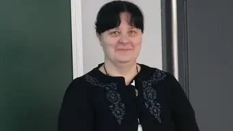 An image of a black-haired woman with bangs in a black cardigan standing against a neutral background.