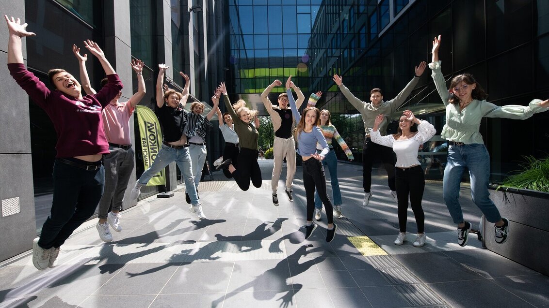 Grupa młodych ludzi - studentów i studentek - podskakuje radośnie. Zdjęcie wykonane na kampusie AGH.