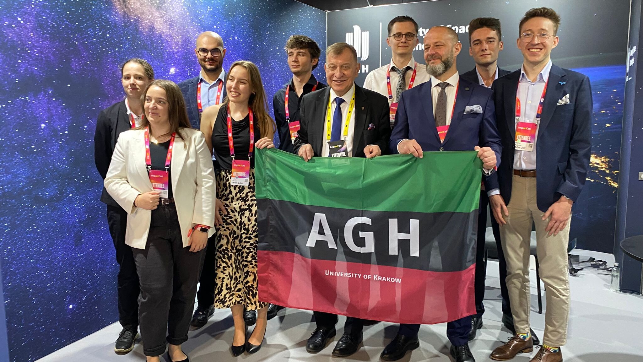 A group photograph of AGH University representatives holding a university banner inside the booth of the Faculty of Space Technologies.
