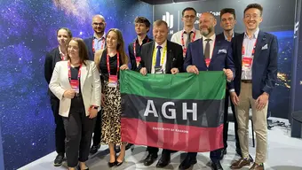 A group photograph of AGH University representatives holding a university banner inside the booth of the Faculty of Space Technologies.