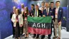 A group photograph of AGH University representatives holding a university banner inside the booth of the Faculty of Space Technologies.