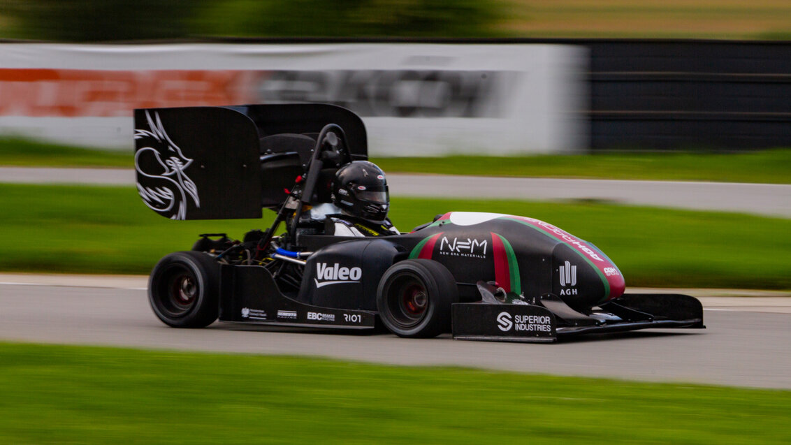 Zdjęcie bolidu wyścigowego z czarnym kolorze na torze.
