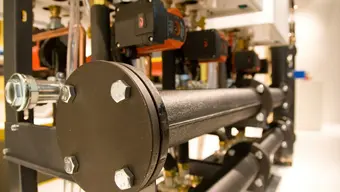 Elementy instalacji technicznej z widocznymi stalowymi rurami, zaworami i pompami.