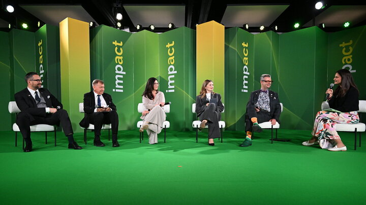 Six panellists sitting on a green stage with the logotype of 'impact' on panelling behind them.