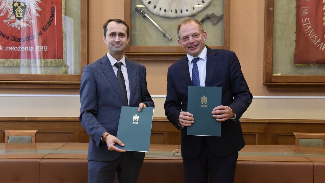 Two men in suits posing for a picture. They hold dark-green folders with the AGH UST logo in gold.