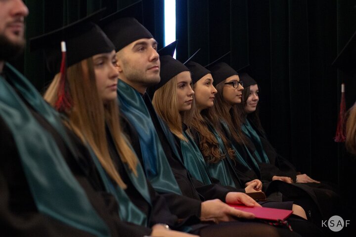 Zdjęcie z uroczystości. Zbliżenie na siedzących w rzędach absolwentów i absolwentki.