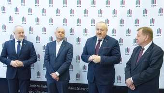 An image of four older men staing in front of a white backdrop with numerous logos of the AGH University