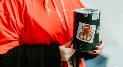 Image of a woman in a red t-shirt holding a green money box with a sticker with a teddy bear