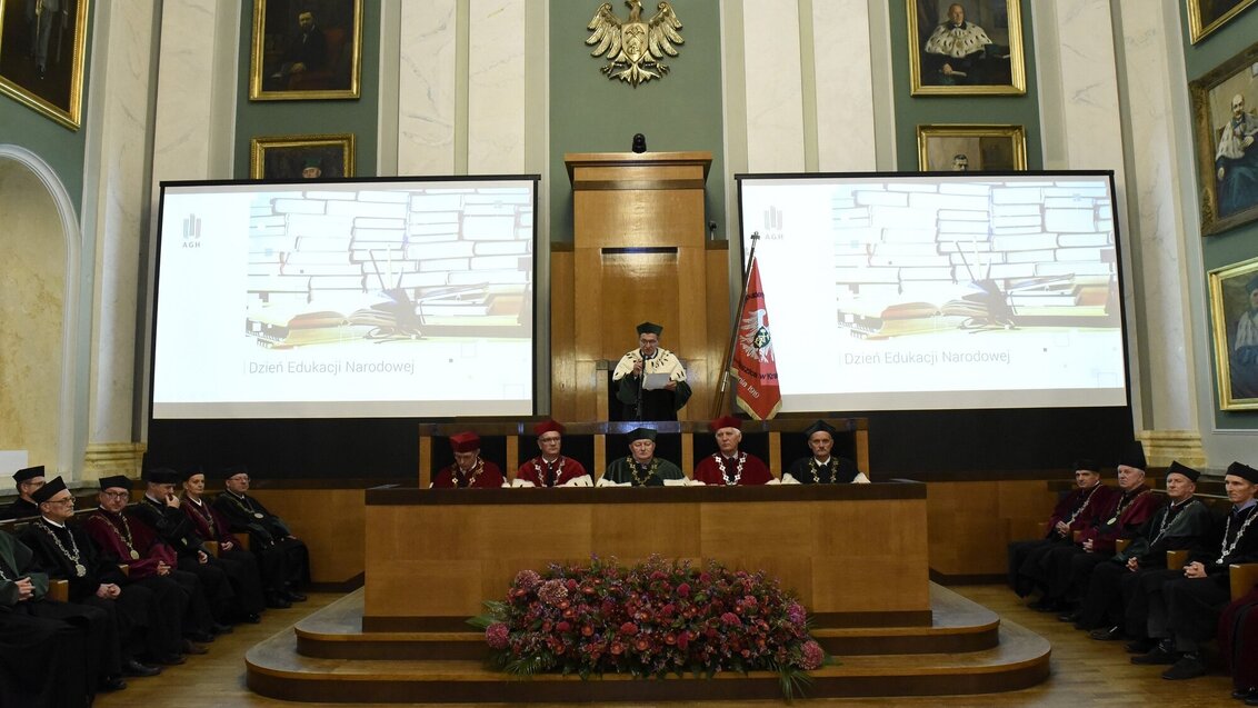 The interior of ceremonial hall with two large presentations, portraits of rectors on the walls, the current AGH University Rector standing and speaking in the middle of the room