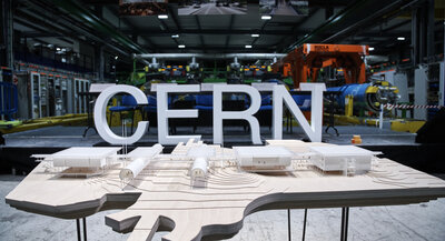 Makieta architektoniczna kompleksu naukowego CERN umieszczona na stole w hali laboratoryjnej, na tle dużych liter „CERN” oraz infrastruktury badawczej.
