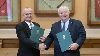Dwóch eleganckich mężczyzn trzymających teczki stoi w sali konferencyjnej