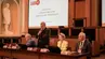 Uczestnicy posiedzenia Konferencji Rektorów Polskich Uczelni Technicznych przy stole prezydialnym. Jedna z osób przemawia do mikrofonu.