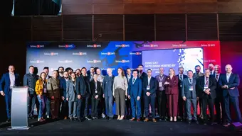 Grupa ok. 30 osób stojących na scenie, uczestników konferencji, za nimi baner z grafiką wydarzenia