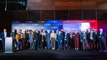 Grupa ok. 30 osób stojących na scenie, uczestników konferencji, za nimi baner z grafiką wydarzenia