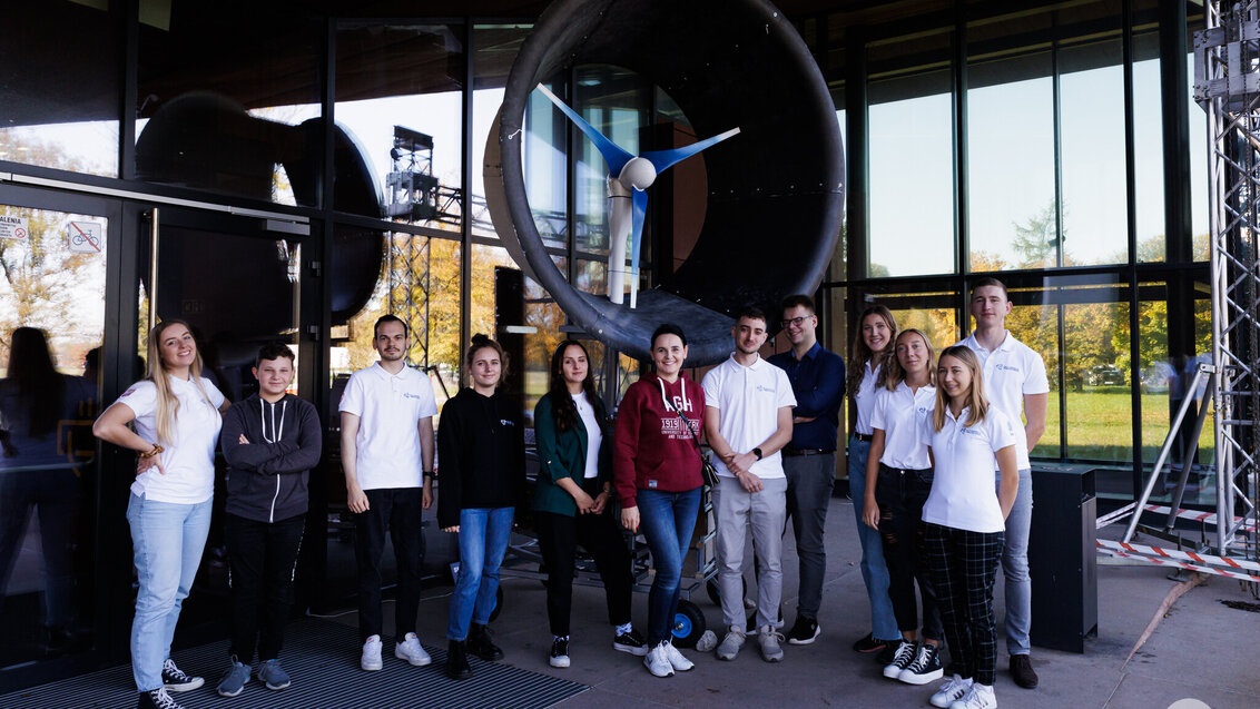 A coloured photo showing members of the Eko-Energia Student Research Club. Behind them, there is a large wind turbine.