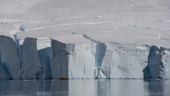 Ściana lodowca opadająca do wody. Na tle ściany widoczna jest mała łódź motorowa z ludźmi na pokładzie. Porównanie proporcji ściany i łodzi pozwala przekonać się, jak ogromny jest rozmiar ściany.