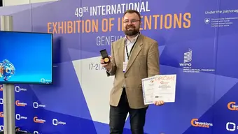 Image of Bartosz Pańtak posing with an award in front of a backwall at the exhibition of inventions